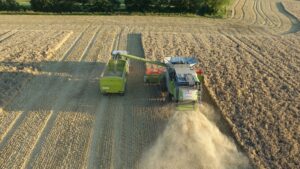 Drone captures a harvester unloading wheat into a trailer in a rural field.